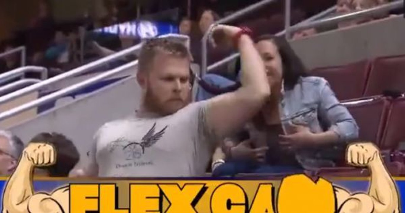 Er zeigt der Kamera seine Muskeln, als die Frau hinter ihm ihre Jacke auszieht