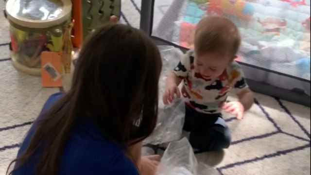 Sweet toddler giggles uncontrollably as his mother pops the packing bubbles