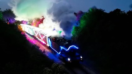 Steam train decked out in vibrant neon lights passes through countryside