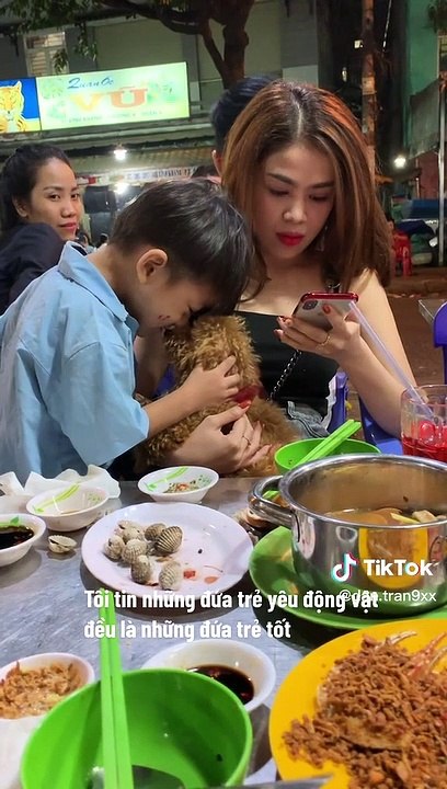 Cậu bé bán hàng rong nâng níu chú cún của khách