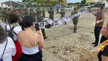 Manifestante tentam ler carta enquanto militares marcham e tocam instrumentos