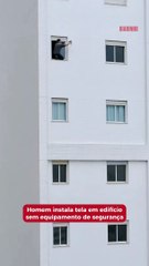 Homem instala tela em edifício sem equipamento de segurança