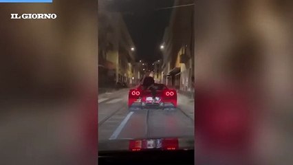 Follia a Milano, parla al telefono seduto sul cofano di una Ferrari in movimento