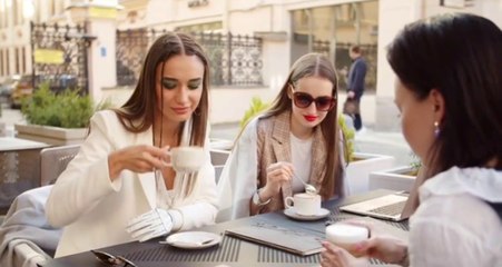 Three young women drink coffee, share events, smile, and have fun with their music