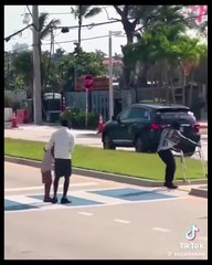 Two men carry an old woman across a busy highway crosswalk