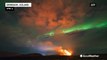 Northern lights dance in night sky over erupting volcano