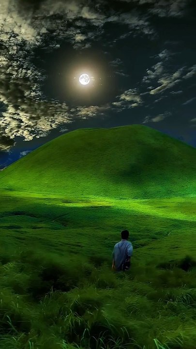 Nature _ Vacation _ adventure - A lone figure stands in a lush_ green meadow under a mesmerizing night sky. The moon shines brightly_ casting an ethereal glow over the rolling hills_ while clouds drift peacefully in the sky. Th