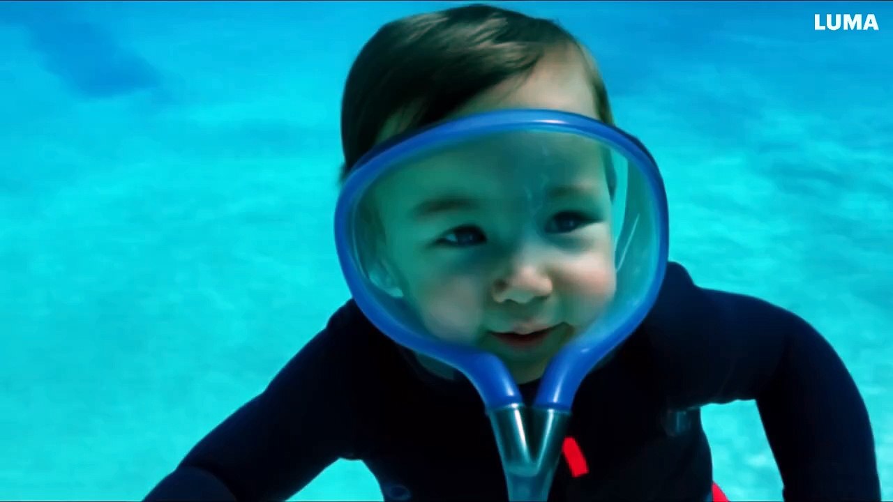 A baby laughing underwater, wearing a scuba diving suit, her expression denotes calm and happiness-26ddf7