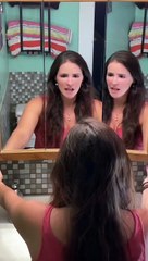 Une jeune femme chante du métal devant son miroir dans la salle de bain.