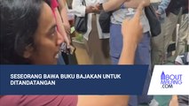 SESEORANG MEMBABAWA BUKU BAJAKAN UNTUK DITANDATANGAN PENULIS ASLINYA