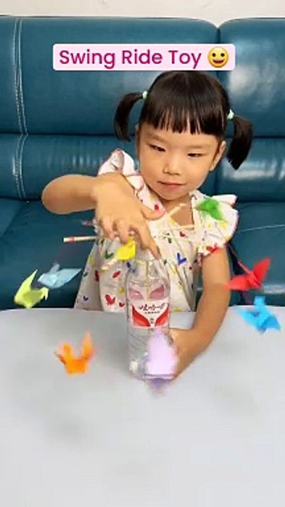 Creating a DIY swing ride toy with just a few simple materials! First, thread an elastic hair band through a plastic bottle, then place an upside-down bottle cap at the top. Attach a wooden stick circle to the bottl