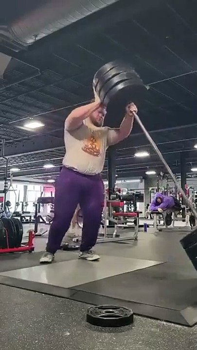Man lifts 405 pound weight from the side, flips it onto his back and does squats with it