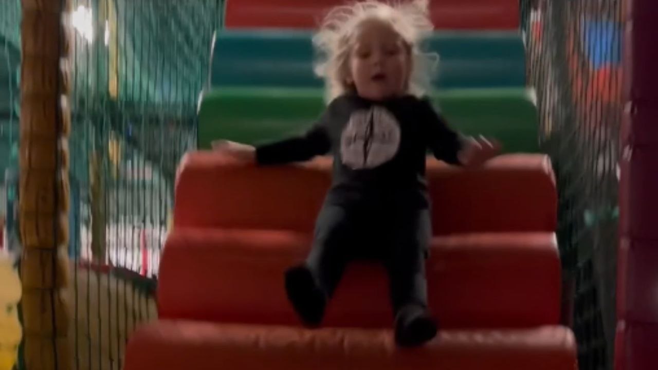 Little boy extends his legs and launches himself down a padded ramp