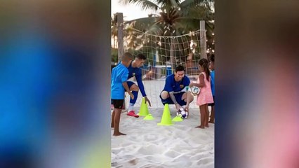 Lionel Messi and Cristiano Ronaldo are on a sunny tropical beach, playing barefoot soccer with a group of children