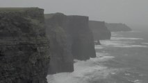 Strong wind forces visitor to cling to a fence at the Cliffs of Moher