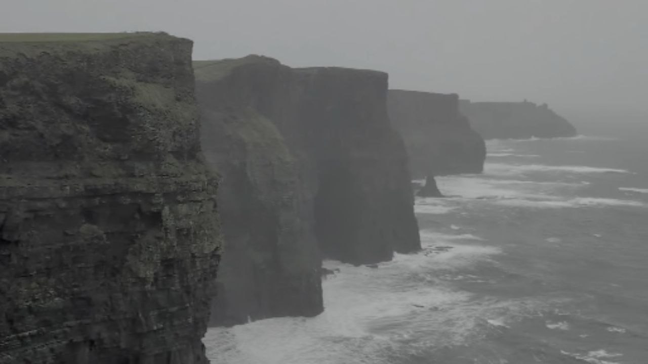 Strong wind forces visitor to cling to a fence at the Cliffs of Moher