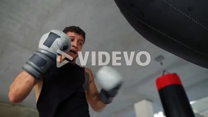 Low angle view male boxer training aggressively with boxing bag