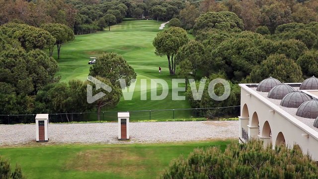 Wide shot of Playing Golfers on Green Fields of Golf Course Facility with Caddie Carts and Trees in Daytime