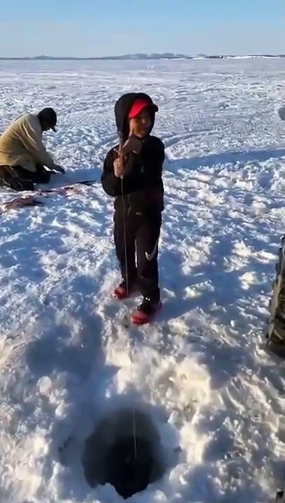 Ce garçon pêche un poisson aussi gros que lui sur un lac gelé