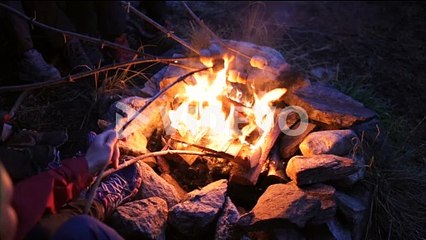campfire - bonfire with stones around in the dark with hands holding marshmallow inside the fire