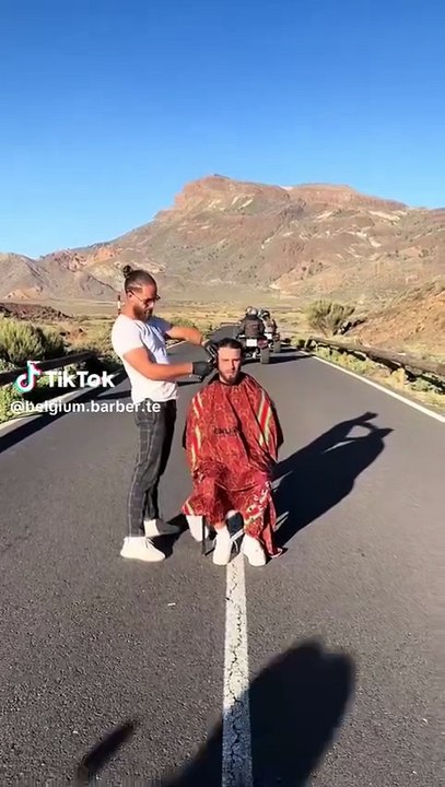 Un barbero belga corta el pelo a un cliente en medio de una carretera en el Teide con quads pasando a su alrededor