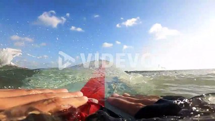 POV, surfer paddling surfboard over ocean wave