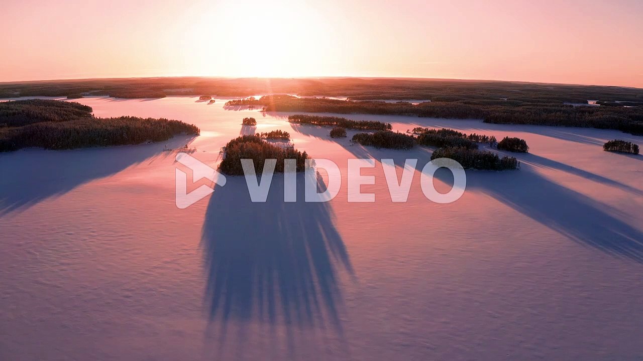 Aerial drone shot of sunset over untouched icy lake with long shadows of small islands