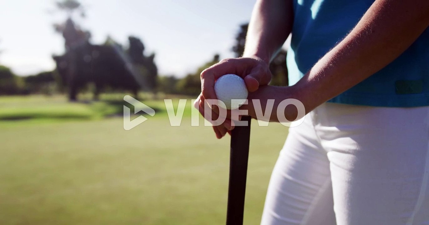 Caucasian female golf player holding a ball and a golf club standing on golf field