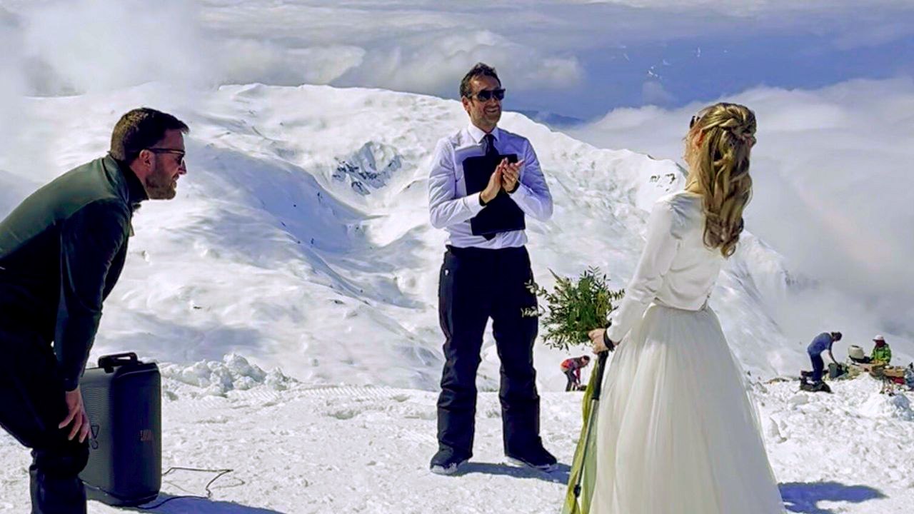 Braut fährt in ihrem Hochzeitskleid auf Skiern den Gang hinunter, um auf dem Berg zu heiraten