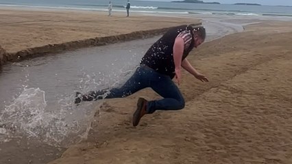 Moment, in dem ein Mann beim Versuch, über einen Strandgraben zu springen, zu kurz kommt und stürzt