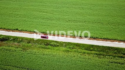 Aerial landscape sideway shot of claret van driving on gravel road between green agricultural fields hungary europe