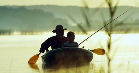 Senior fisherman in hat floating with his grandson in the boat and fishing with a rod in the lake