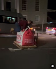 Two men ride a pallet truck down Brecon street