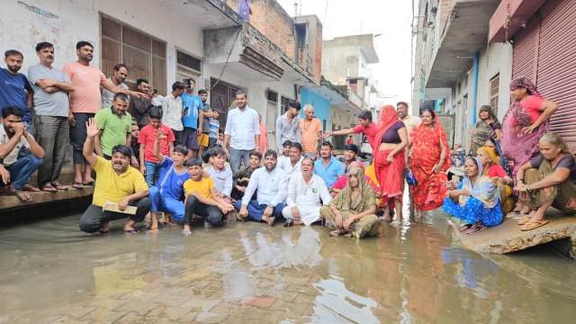 नाला चोक होने से गलियों में भरा पानी, गुस्साए लोगों ने पानी में बैठकर किया प्रदर्शन
