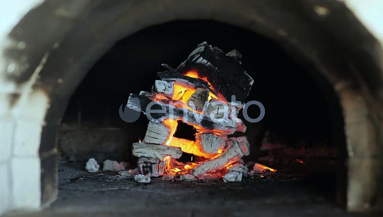 Stack of burning logs collapse and fall inside red hot pizza oven