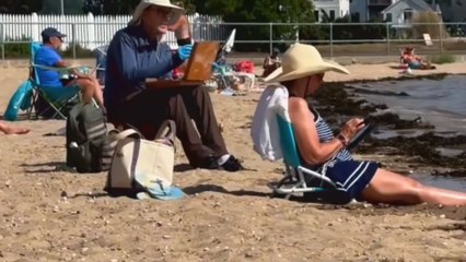 Man paints his wife at the beach while waves dance in the background