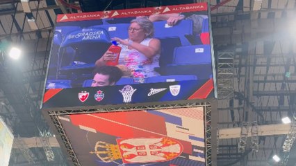 LED screen in basketball arena focuses on lady in crowd preparing and eating a sandwich