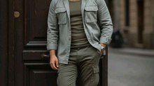 "Casual vibes 💁‍♂️! Guy chillin' by the doorway 🛗 in an olive green outfit 🍃 - shirt, pants, and an open jacket 🔓. Rockin' navy sneakers 🥿 and a sick watch 🕰️. Background's a blurry city street 🌆. #CasualStyle #OliveGreen #StreetChill"
