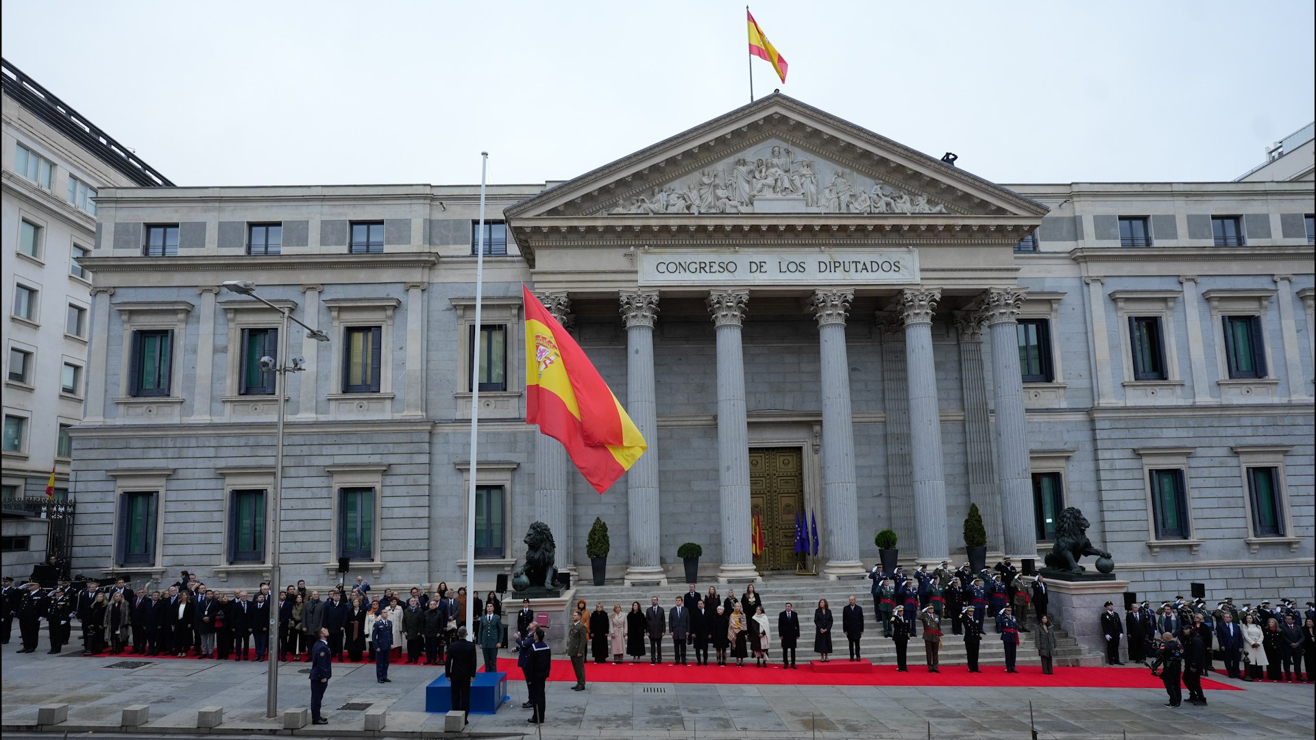 Los actos conmemorativos del 47� aniversario de la Constituci�n Espa�ola arrancaron este s�bado en la madrile�a Carrera de San Jer�nimo con el tradicional y solemne izado de la bandera nacional frente al Congreso de los Diputados,. A las 10:30 horas dio comienzo el evento, que se desarroll� bajo un cielo plomizo, marcando el inicio de la jornada organizada por las Cortes Generales.
El almirante general Teodoro Esteban Calder�n, Jefe de Estado Mayor de la Defensa (Jemad), recibi� a los presidentes de las C�maras, Francina Armengol (Congreso) y Pedro Roll�n (Senado), a la altura de la calle de Cedaceros,. Tras la interpretaci�n del himno nacional en su versi�n corta, los tres dignatarios pasaron revista a la compa��a militar de honores,. Dicha agrupaci�n estaba compuesta por efectivos de los dos ej�rcitos, la Armada y la Guardia Civil.
A continuaci�n, descendieron hacia las escalinatas de la Puerta de los Leones, donde aguardaban los m�ximos responsables de los ej�rcitos, incluyendo al general Amador Ense�at y Berea (Jeme), Francisco Braco (Jema) y almirante general Antonio Pi�eiro (Ajema), junto a la directora de la Guardia Civil, Mercedes Gonz�lez. En un acto de profundo significado, varios efectivos extrajeron la bandera del patio de Floridablanca del Congreso para su izado. Un relator record� el significado de la ense�a nacional, citando textualmente el primer art�culo de la Ley que regula su uso: "La bandera de Espa�a simboliza la naci�n; es signo de la soberan�a, independencia, unidad e integridad de la patria y representa los valores superiores expresados en la Constituci�n". La bandera fue elevada junto a las escalinatas, delante de un ejemplar de la Carta Magna, de nuevo con los acordes del himno nacional de fondo.
La primera parte de la conmemoraci�n, que se celebr� sin p�blico en las calles aleda�as, las cuales amanecieron cerradas debido a un amplio per�metro de seguridad dise�ado por las fuerzas de seguridad,, concluy� con un desfile ante las autoridades,. Adem�s, se leyeron los tres primeros art�culos del Real Decreto que establece el D�a de la Constituci�n.
Finalmente, el Jemad acompa�� a Armengol y Roll�n al interior del Palacio del Congreso tras saludar a los representantes militares y pol�ticos presentes. En el Sal�n de Pasos Perdidos, donde se celebra el acto central, los presidentes comenzaron a recibir a los asistentes. El programa de interior incluy� la interpretaci�n musical de 'Helix Trio'. Posteriormente, alumnos de Primaria de diferentes nacionalidades europeas leyeron en alem�n, franc�s e italiano art�culos clave de la Constituci�n: el 23 (derecho a la participaci�n pol�tica), el 27 (derecho a la educaci�n) y el 48 (dedicado a la juventud). La presidenta del Congreso, Francina Armengol, pronunciar� el discurso final de la jornada. Cabe destacar que, como en ediciones previas, no se esperaba la asistencia de diputados de Vox, Junts, ERC, EH Bildu, PNV y BNG a la recepci�n.
