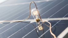 A close-up cinematic shot of a small glowing bulb running directly on a solar panel. The solar panel is placed outdoors in sunlight, and as sunlight hits the panel, the tiny bulb turns on and shines softly. Show clear wiring