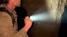 A man holding a flashlight discovers the entrance of a dark underground cave and slowly walks inside.2