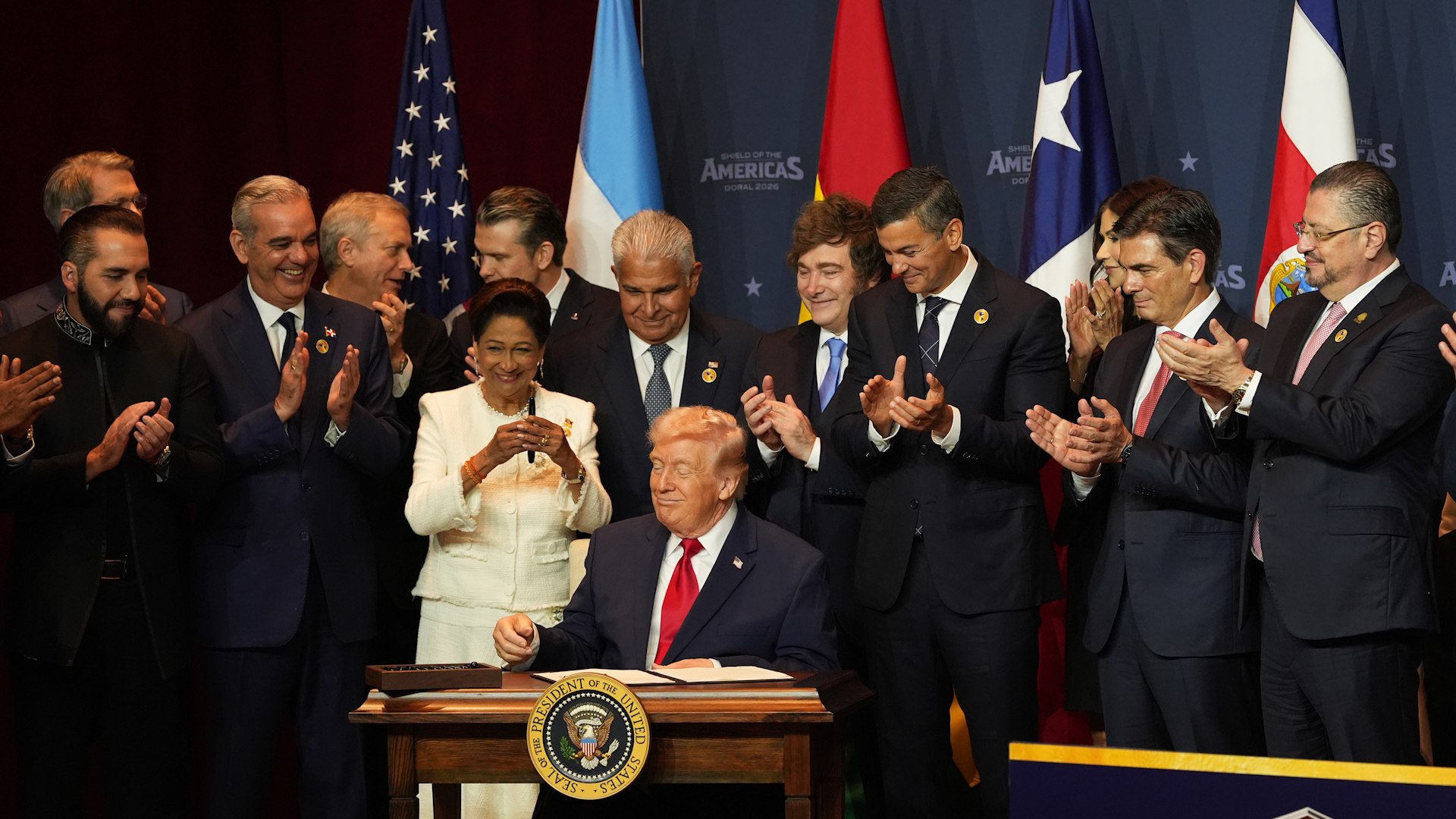 El panorama geopol�tico de las Am�ricas ha dado un vuelco definitivo este s�bado en Miami. En una cumbre que evoca los tiempos de la Guerra Fr�a pero con una est�tica de superh�roes, el presidente de Estados Unidos, Donald Trump, ha presentado su nueva estrategia para la regi�n: la "Doctrina Donroe" (una actualizaci�n de la Doctrina Monroe con la 'D' de Donald). Desde su hotel en el Doral, rodeado de una decena de mandatarios afines, el l�der republicano ha dejado clara su hoja de ruta: mano dura militar contra el narcotr�fico y una distancia cultural insalvable, confirmando que no tiene intenci�n alguna de hablar el idioma de sus aliados.
Bajo el nombre de "Shield of the Americas" (Escudo de las Am�ricas) y con una iconograf�a que, seg�n los presentes, recordaba al Capit�n Am�rica, Trump ha formalizado una alianza b�lica sin precedentes. El objetivo central es la creaci�n de una fuerza conjunta para combatir el crimen organizado transnacional.
"En este d�a hist�rico nos reunimos para anunciar una nueva coalici�n militar para erradicar los c�rteles criminales que azotan nuestra regi�n. Llamamos a esta alianza militar la Coalici�n Antic�rteles de las Am�ricas", proclam� el mandatario ante l�deres como el argentino Javier Milei o el salvadore�o Nayib Bukele. Trump justific� esta movilizaci�n citando �xitos recientes como la captura de Nicol�s Maduro &mdash;a quien EE. UU. se�ala como cabecilla del C�rtel de los Soles&mdash; y la ca�da de Nemesio Oseguera 'El Mencho', l�der del C�rtel Jalisco Nueva Generaci�n.

A pesar de la sinton�a ideol�gica con los mandatarios presentes &mdash;entre los que tambi�n figuraban Rodrigo Paz (Bolivia) o Luis Abinader (Rep�blica Dominicana)&mdash;, Trump no suaviz� su discurso nacionalista. En un momento que provoc� risas entre los asistentes, el presidente estadounidense cerr� la puerta a cualquier integraci�n ling��stica.
"No voy a aprender su maldito idioma. No tengo tiempo. No tengo problema con los idiomas, pero no voy a dedicar tanto tiempo a aprender el suyo", afirm� tajante, subrayando que prefiere confiar en la figura de un buen int�rprete para sus negociaciones con l�deres como Xi Jinping o Vlad�mir Putin. Incluso brome� sobre la "ventaja ling��stica" de su secretario de Estado, Marco Rubio, quien s� domina el espa�ol por sus ra�ces cubanas.
La cita en el club de golf de Florida no ha sido una reuni�n de toda la regi�n, sino un c�nclave de la derecha latinoamericana. En un gesto cargado de intenci�n pol�tica, la Casa Blanca evit� invitar a los presidentes de las tres principales potencias progresistas del continente: M�xico, Brasil y Colombia.
Con esta "Doctrina Donroe", Trump busca blindar el hemisferio bajo el paraguas de la inteligencia y el poder de fuego estadounidense, dejando claro que, aunque sus aliados pongan el terreno y las tropas, la comunicaci�n y las �rdenes se seguir�n dando exclusivamente en ingl�s.