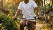 A young boy happily rides his bicycle down a peaceful village road during sunset, with the golden light casting long shadows. Coconut trees gently sway in a soft breeze as