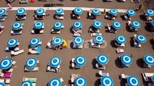 A Drone Flies Over Even Rows of Bright Blue Beach Umbrellas Illuminated By the Sun