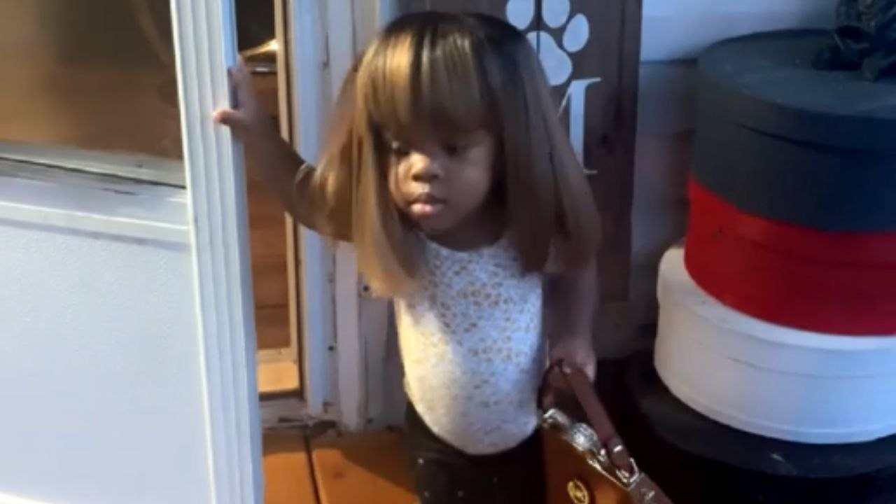 Charming young child flaunts impressive fashion sense with wig and oversized handbag