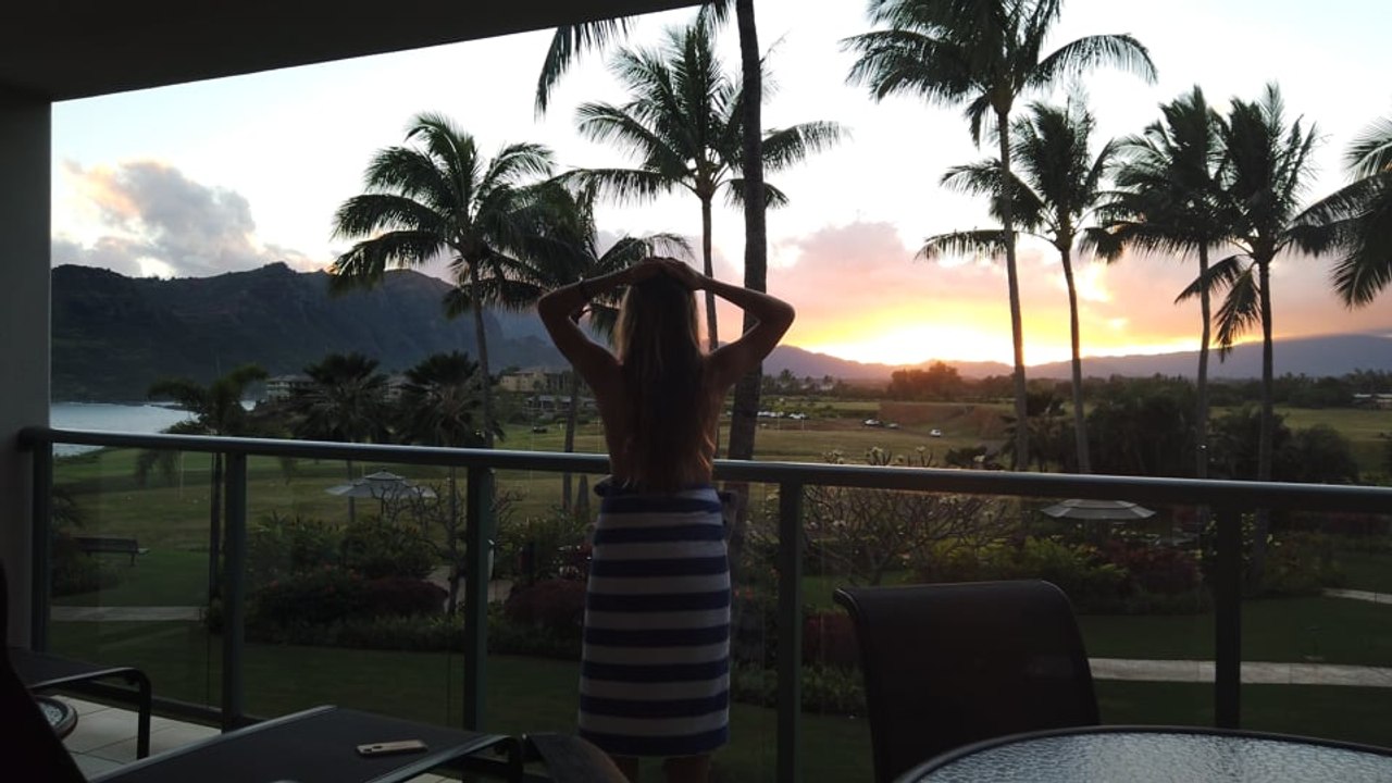 A Woman Stands Peering out at a Stunning Tropical Island Resort, A Beautiful Sunset and Mountains in the Background
