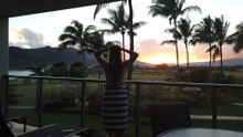 A Woman Stands Peering out at a Stunning Tropical Island Resort, A Beautiful Sunset and Mountains in the Background