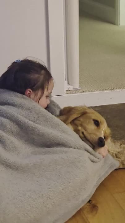 Little Girl and Puppy Cuddle Under Blanket