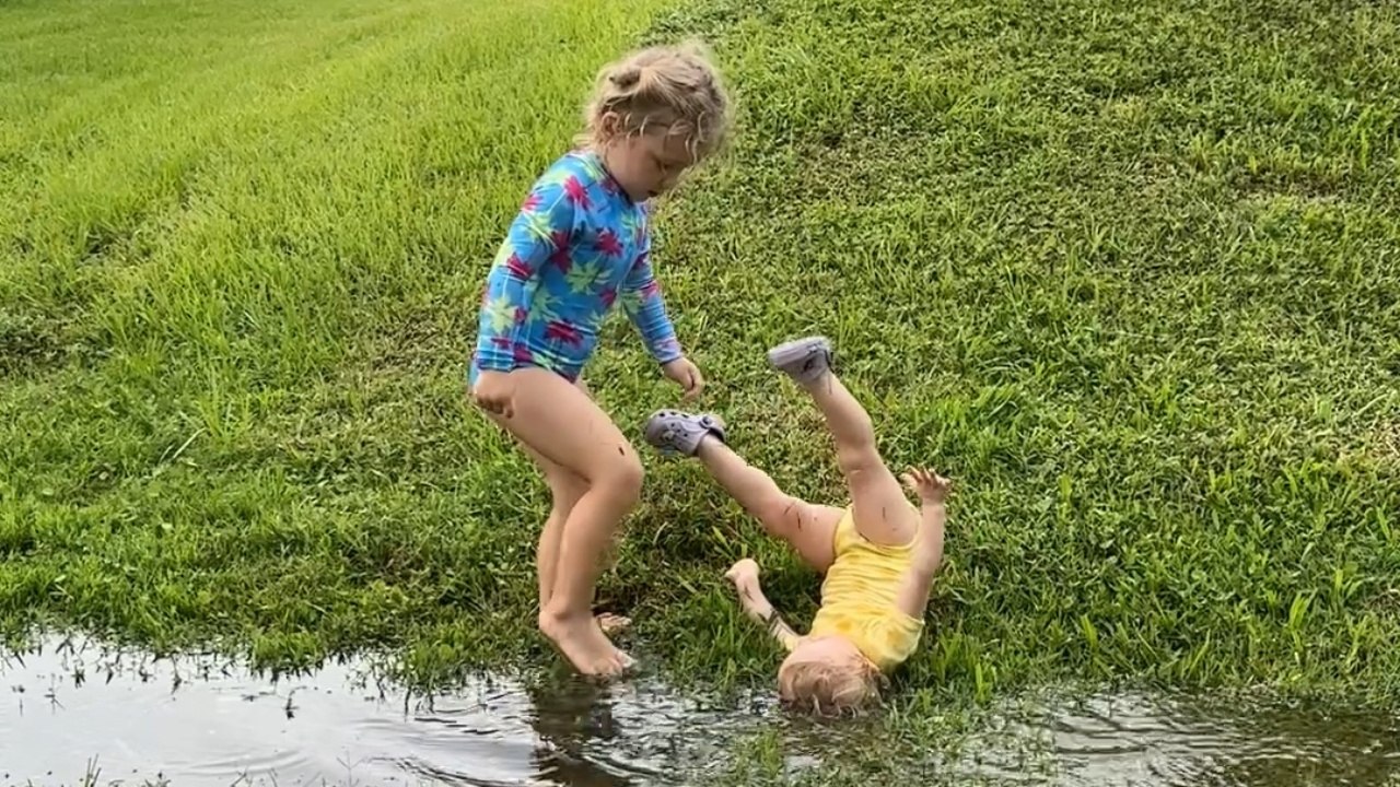 Young Sisters Playfully Splash in Lawn Puddle Post-Rain