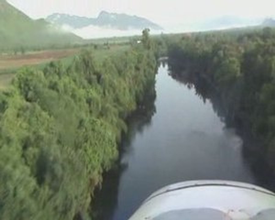 A sport aircraft flying low along a stream